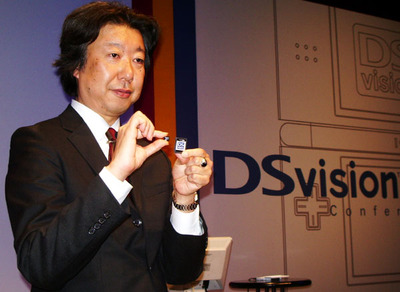 専用アダプタおよび専用microSDを手にする澤居氏。専用のmicroSDには個別のIDが割り振られ,それを用いて著作権保護など,コピーガードを実現していくとのこと。 専用アダプタおよび専用microSDを手にする澤居氏